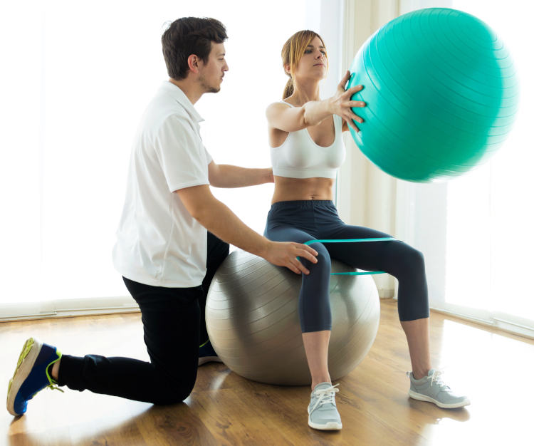 Physiotherapist helping patient to do exercise on fitness ball i